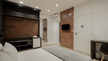 A modern hotel room with a bed, a desk, a TV, and a minibar.