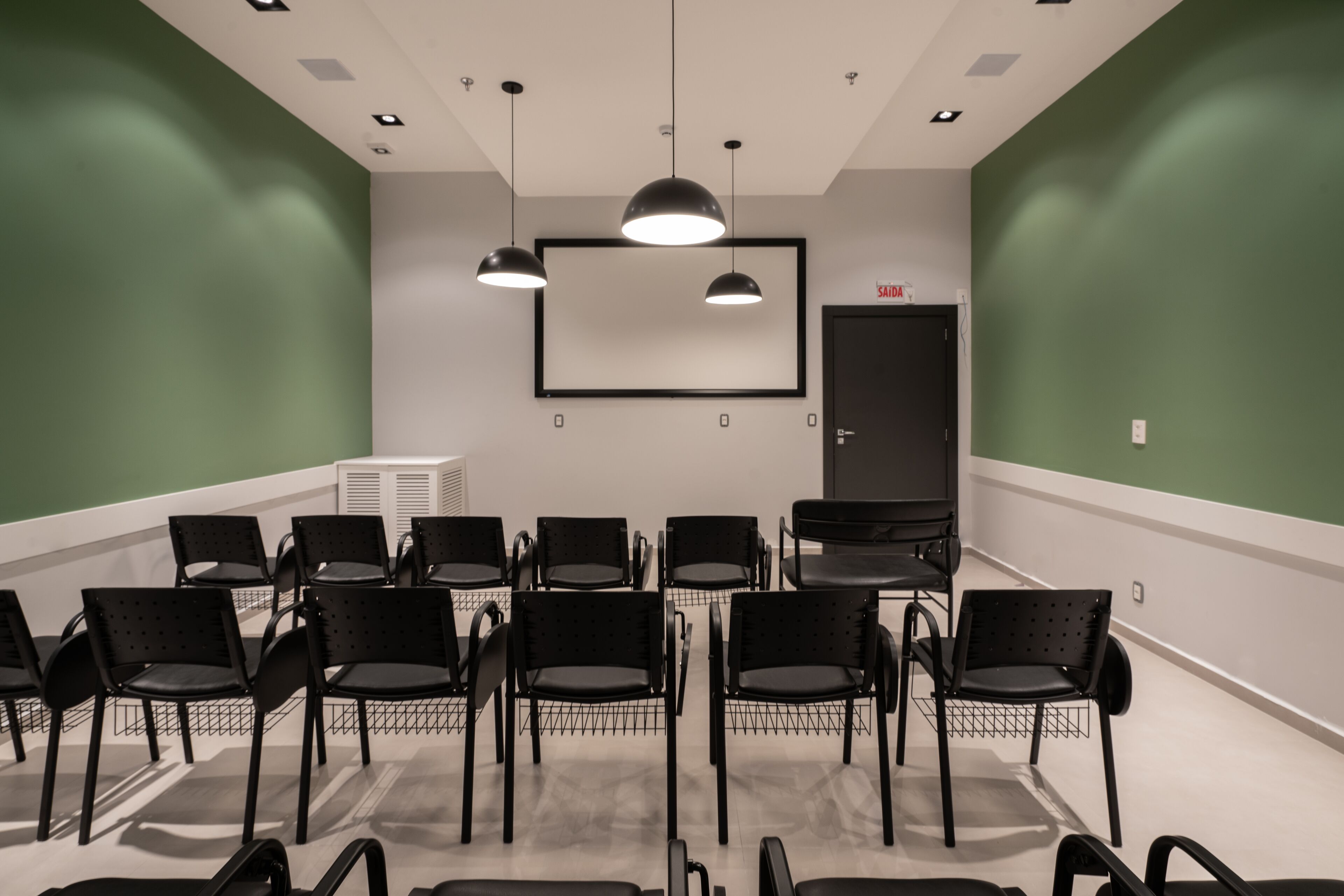 A conference room with a whiteboard, black chairs, and pendant lighting.