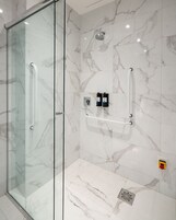 Un baño moderno con cabina de ducha de vidrio, baldosas de mármol, cabezal de ducha de mano y dos dispensadores de jabón.