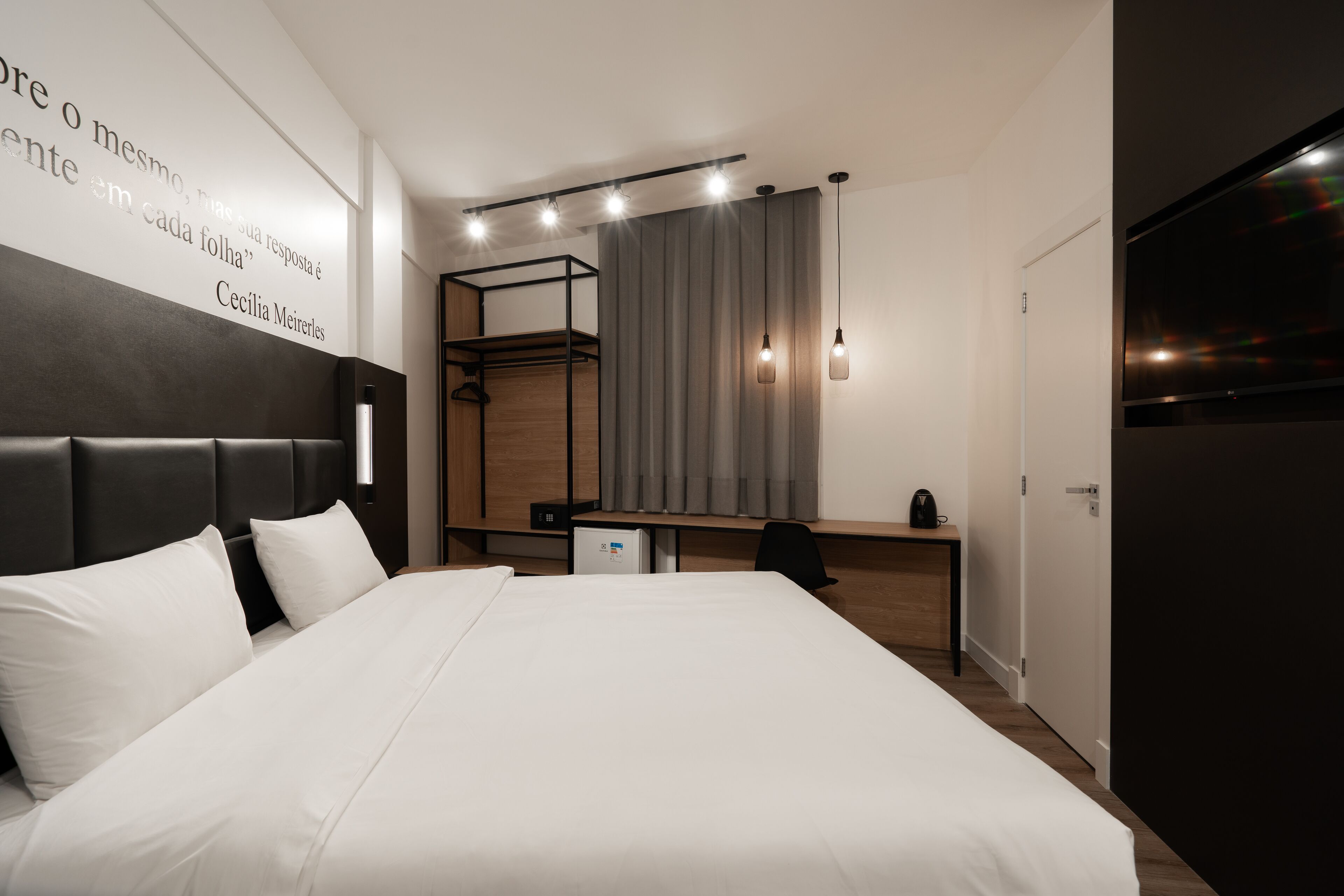 A modern hotel room with a large bed, a desk, a wardrobe, and a TV.
