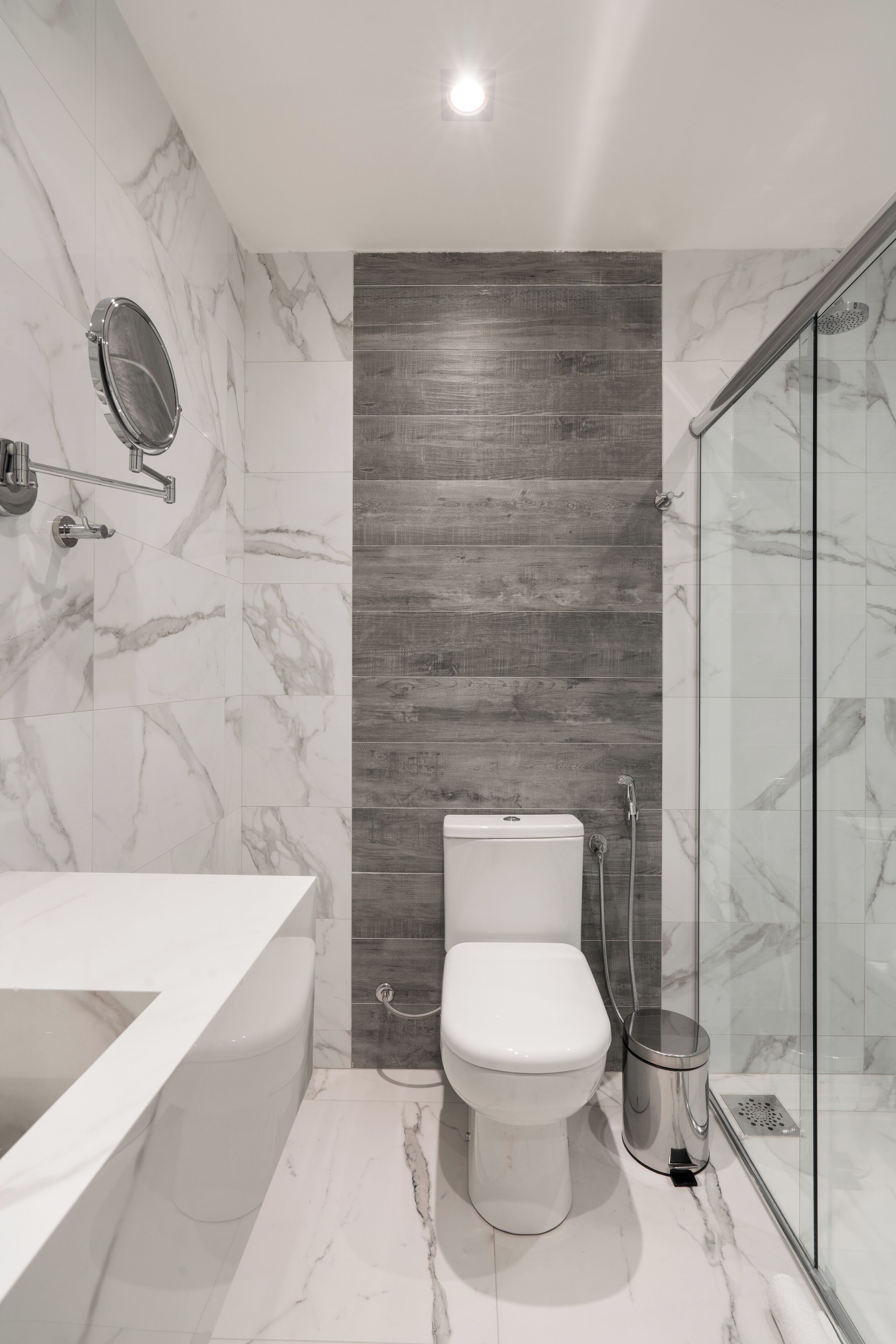 Un baño moderno con inodoro blanco, cabina de ducha de vidrio y suelo de baldosas de mármol.