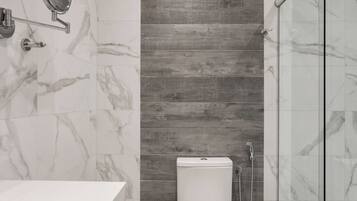 Un baño moderno con inodoro blanco, cabina de ducha de vidrio y suelo de baldosas de mármol.