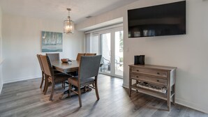 A dining area with a wooden table and chairs, a chandelier, a painting, and a TV mounted on the wall.