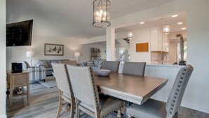 A dining area with a large wooden table, upholstered chairs, and pendant lighting.