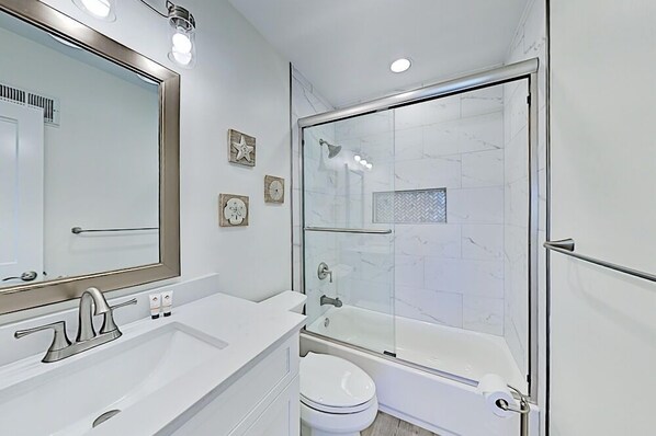 Une salle de bain moderne avec un grand miroir, un lavabo blanc, des toilettes et une douche séparée par une paroi de verre.