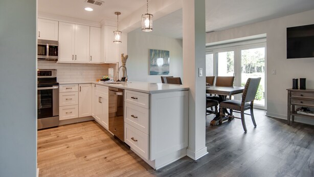 A modern kitchen with white cabinets, stainless steel appliances, and a dining area with a table and chairs.