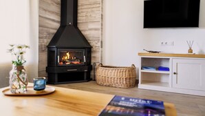 Una sala de estar acogedora con chimenea, televisor montado en la pared, una mesa de madera y un armario blanco.