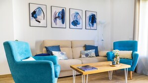 Un salón con un sofá color beige, dos sillones azules, una mesa de centro de madera y cuatro cuadros abstractos en la pared.