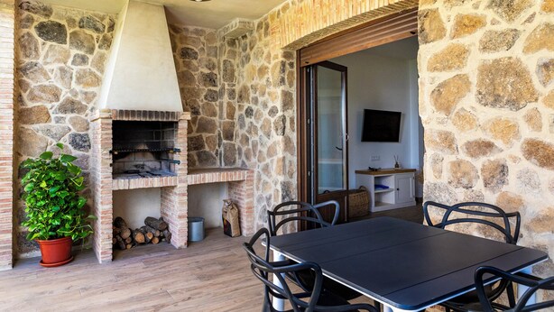 Un espacio al aire libre para comer con paredes de piedra, una chimenea de ladrillo, una planta en maceta y una mesa con sillas.