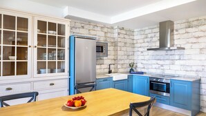Una cocina con armarios azules, un refrigerador de acero inoxidable, un microondas, una estufa y una mesa de comedor de madera con fruta.