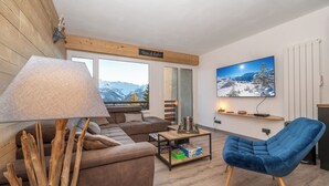 A modern living room with a brown sofa, a blue armchair, a wooden coffee table, and a large TV on the wall.