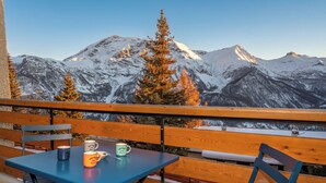 A balcony with a table and chairs, overlooking snow-covered mountains and a clear sky.