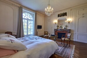 A bedroom with a large bed, a fireplace, a chandelier, and a view of the outdoors. - Large family Suite garden view (Barbeville)