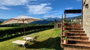 Una terraza con mesa y sillas, un gran paraguas y una escalera de piedra que sube a un nivel superior.