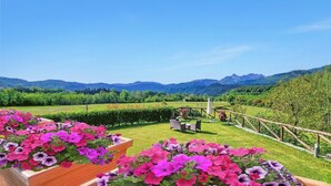 Un jardín con cerca de madera, muebles de exterior y vistas a colinas y montañas verdes.