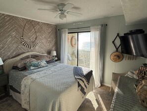 A bedroom with a bed, a ceiling fan, a window with curtains, and a wall-mounted TV. - Ocean Front Condo! (North Myrtle Beach)
