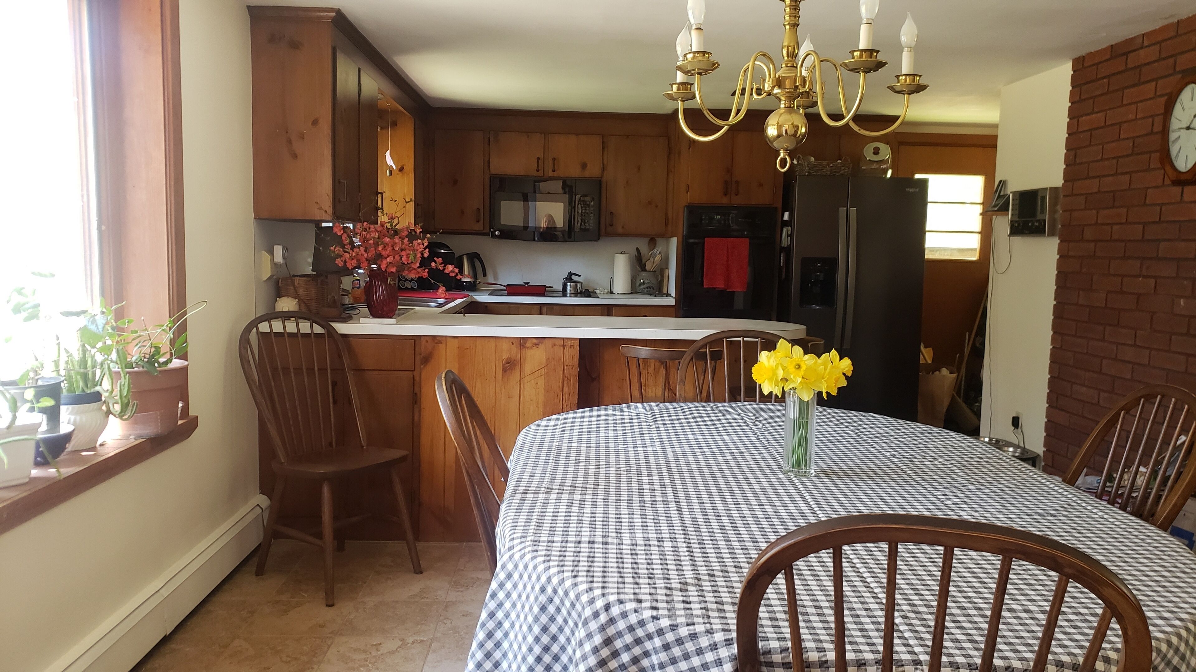 A kitchen with wooden cabinets, a black refrigerator, and a dining area with a checkered tablecloth and chairs.