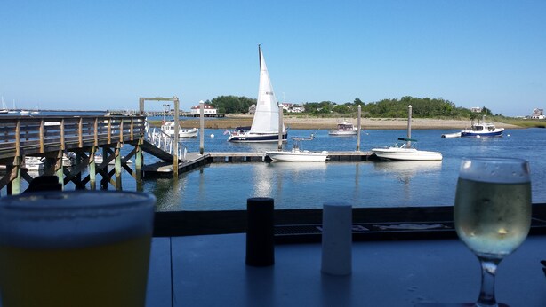 Une vue d’une marina avec des bateaux amarrés, un voilier au centre et un verre de bière posé sur une table.
