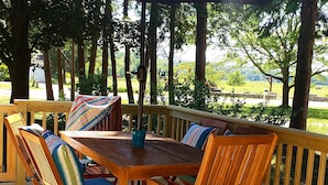 Une terrasse extérieure en bois, dotée d’une table et de chaises, entourée d’une rambarde, et d’un grand parasol offrant de l’ombre.