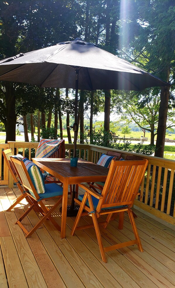 An outdoor wooden deck with a table and chairs, a large umbrella, and a view of a green landscape.