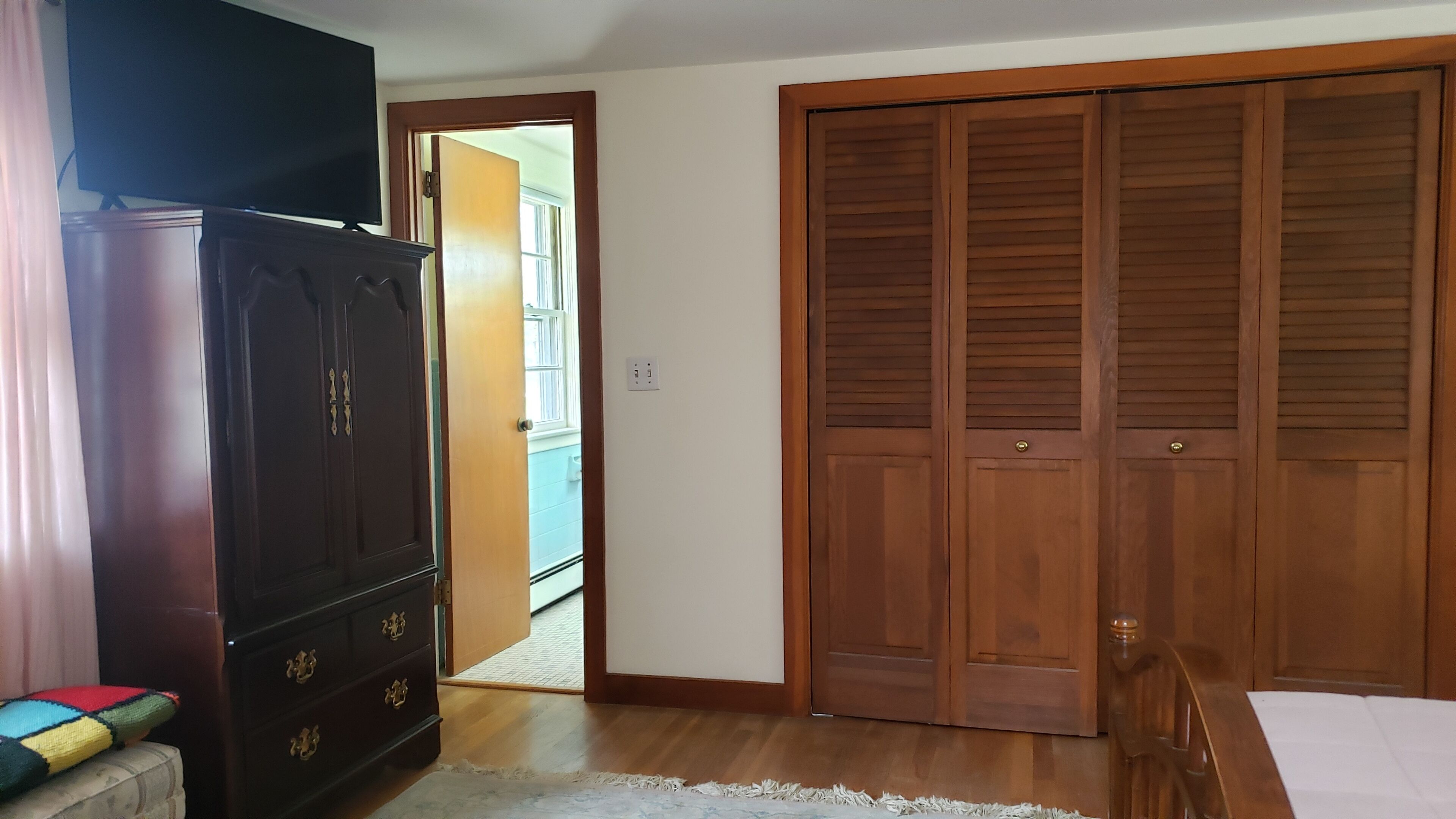 A room with a wardrobe, a bed, and a door leading to another room.
