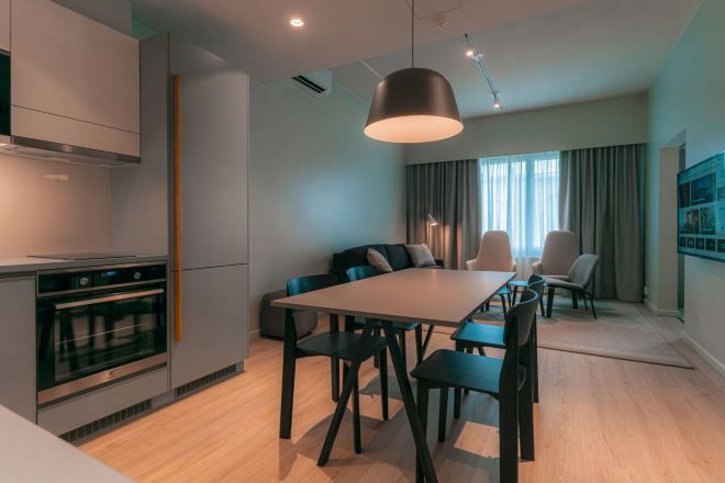 Una cocina moderna con horno empotrado, un comedor con una mesa grande y sillas, y una lámpara colgante de gran tamaño.