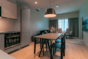 Une cuisine moderne dotée d’un four encastré, d’un coin repas avec une longue table et des chaises, et d’un grand luminaire suspendu.