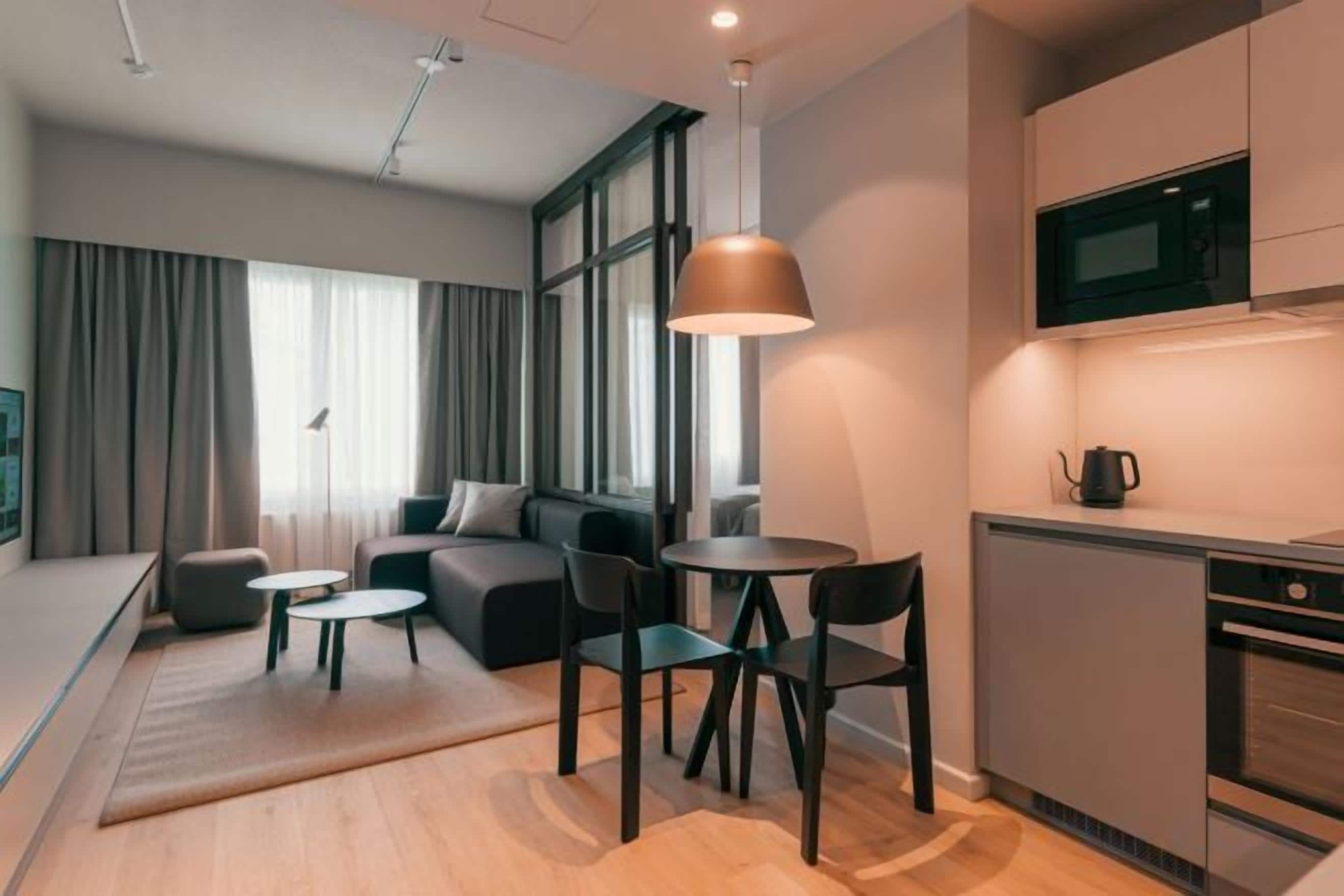 A modern living room with a sofa, coffee table, and chairs, a kitchen with a microwave, and a dining area with a table and chairs.