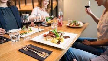 Een eettafel met borden eten, glazen wijn en bestek.