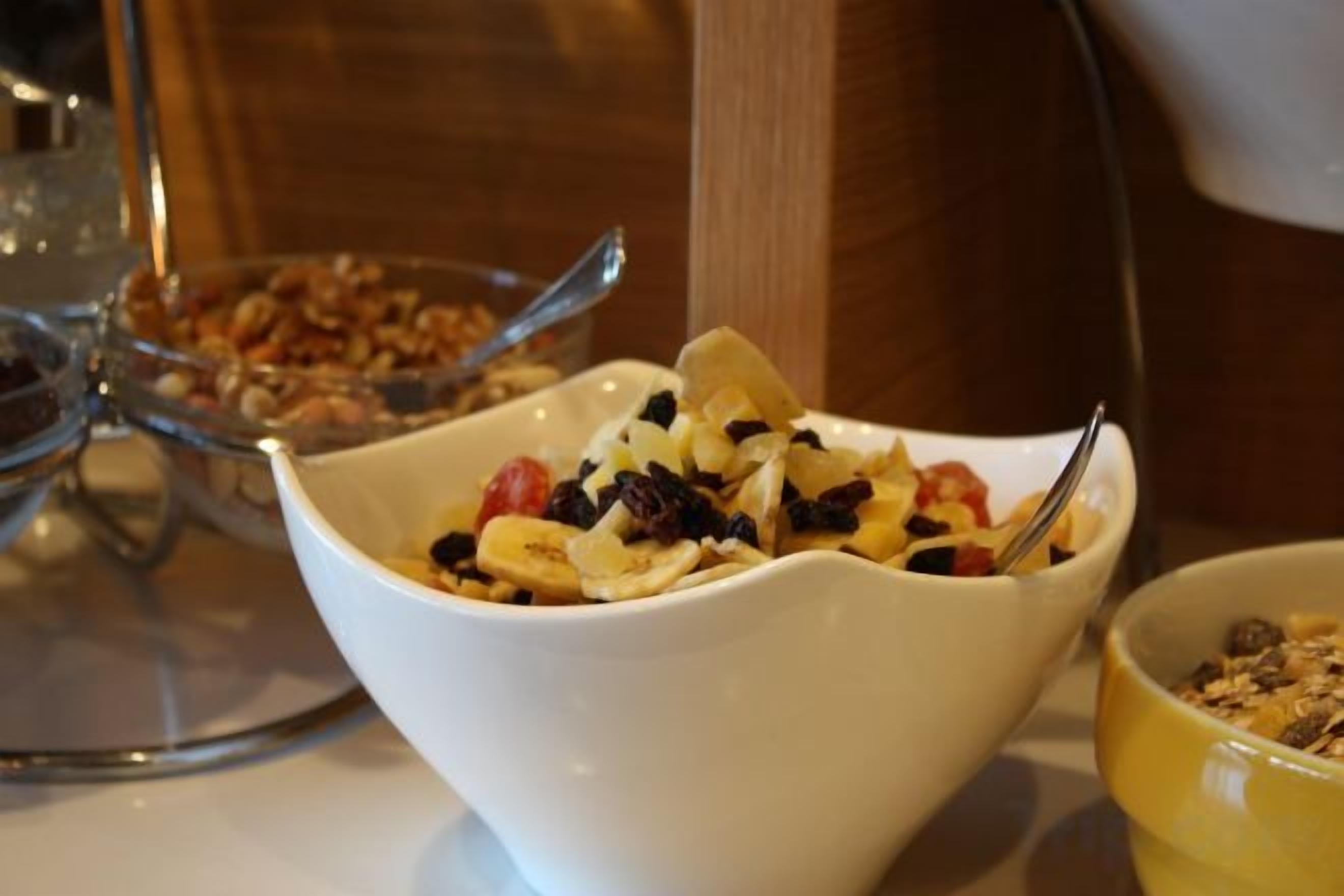 A white bowl with granola and fruit on a table.