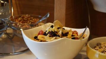 A white bowl with granola and fruit on a table.