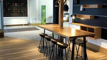 Un intérieur moderne avec une table en bois et des tabourets de bar, un mur foncé agrémenté d’étagères et un présentoir vert contenant des informations.