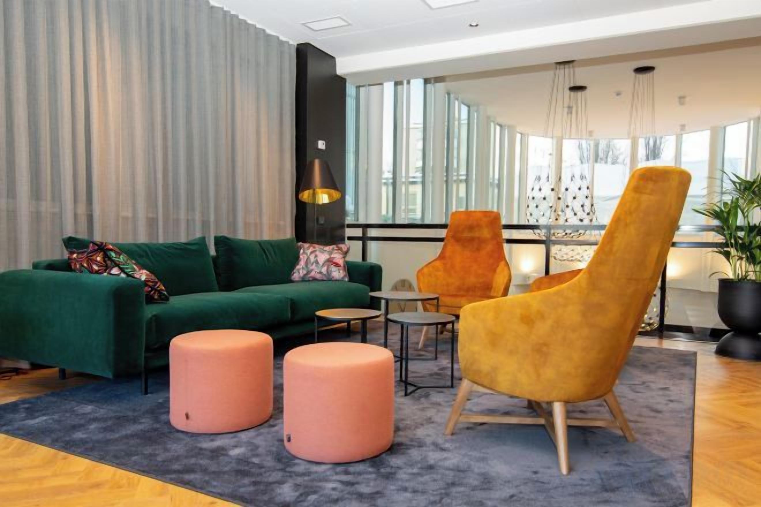 A modern lounge area with a green sofa, a yellow armchair, and two pink ottomans.