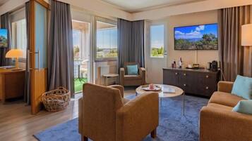 Habitación de hotel con sofá, sillón, televisor y balcón con vistas.