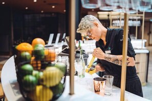 Une personne prépare une boisson au bar, avec un saladier de fruits et des verres disposés sur le comptoir.