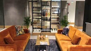 Un hall d’hôtel moderne avec deux canapés orange moelleux, une table basse centrale et, au fond, un présentoir à vin.