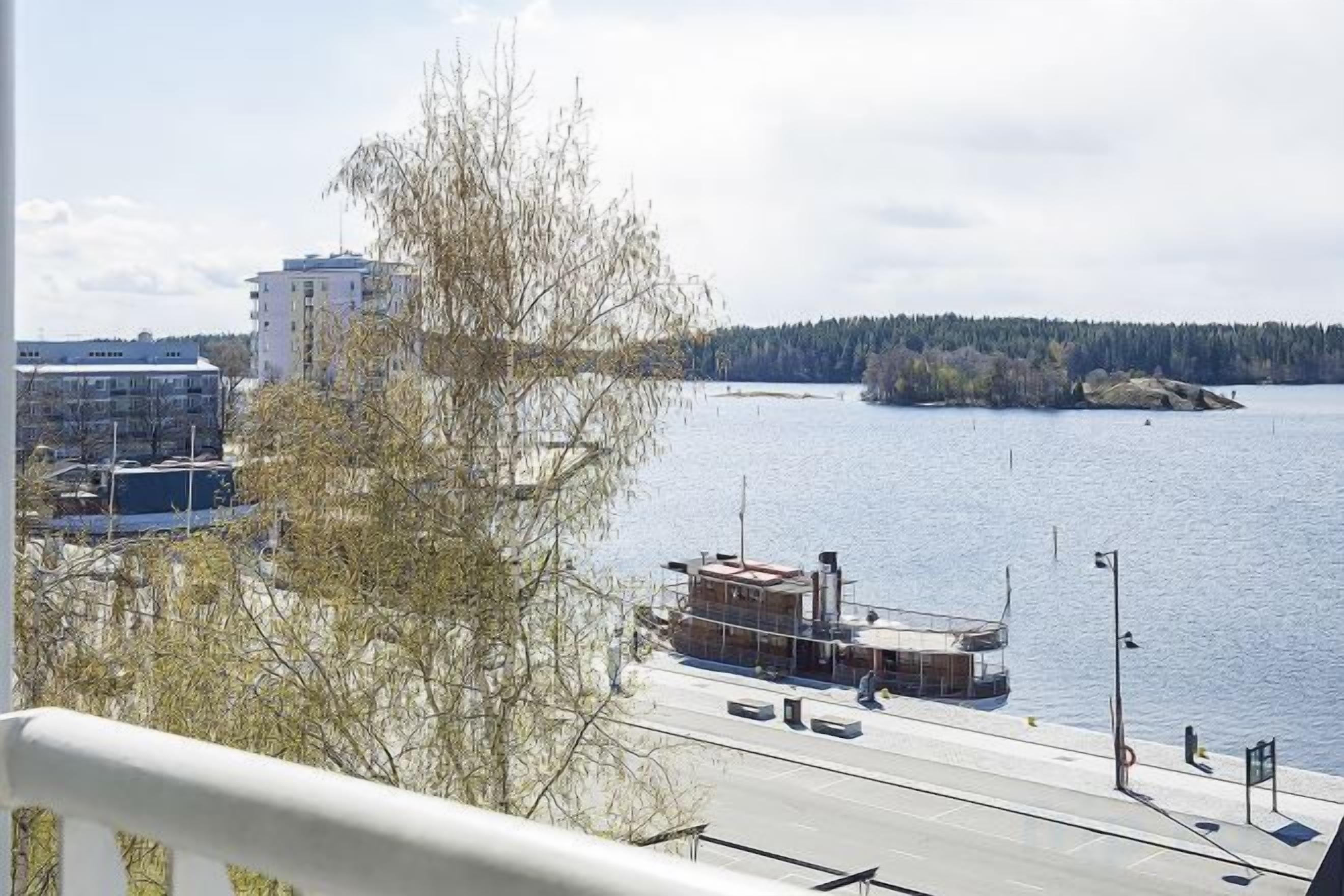 Blick auf das Wasser mit einem Gebäude, einem Steg und einem Baum.