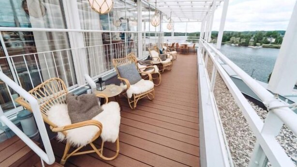 Une terrasse extérieure couverte, dotée de chaises et de tables en osier, qui offre une vue sur une étendue d’eau.