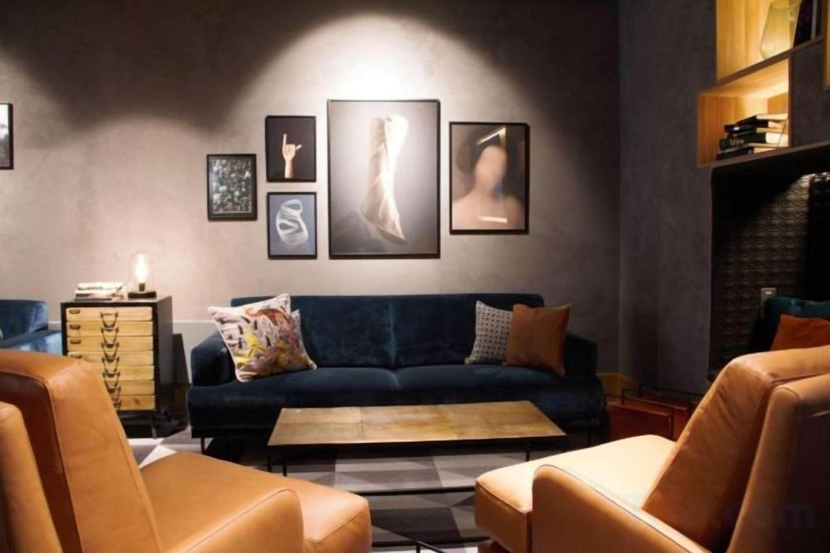 A modern living room with a dark blue sofa, two leather armchairs, a coffee table, and a sideboard with drawers.