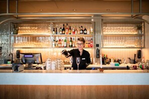 Een bar met een bartender, flessen, glazen en een kassa.