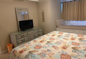 Una camera da letto con un letto, una cassettiera, una televisione e una finestra con tende.