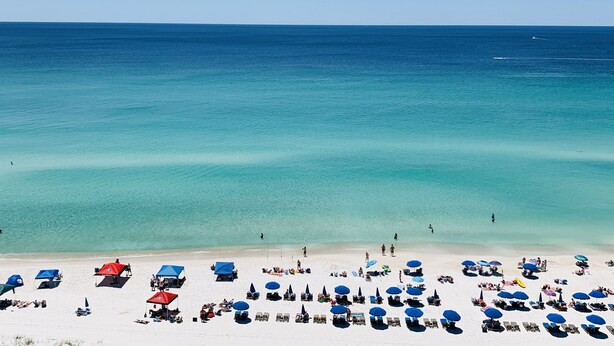 A beach with rows of sun loungers and umbrellas, a clear blue sea, and a sandy shore. - Cooks Beach Getaway LLC (Panama City Beach)
