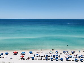 A beach with rows of sun loungers and umbrellas, a clear blue sea, and a sandy shore.