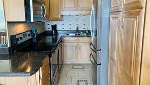 A kitchen with wooden cabinets, stainless steel appliances, a microwave, and a coffee maker. - Cooks Beach Getaway LLC (Panama City Beach)