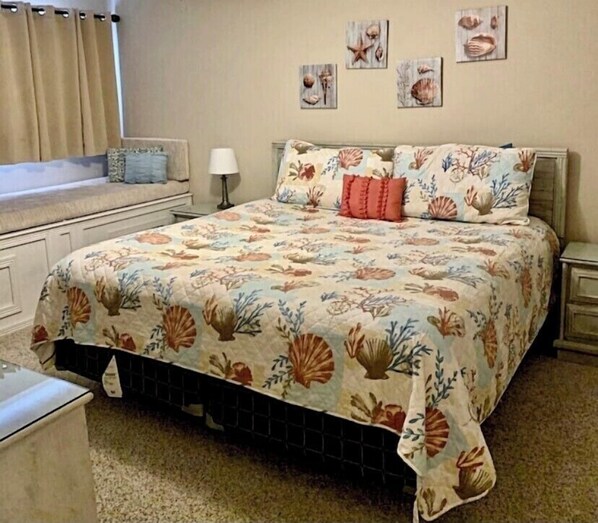 A bedroom with a floral bedspread, a nightstand, a lamp, and wall art. - Cooks Beach Getaway LLC (Panama City Beach)