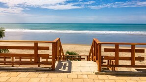 A beach view with wooden railings and a paved walkway leading to the shore. - Family_friendly beach house  (Jama)
