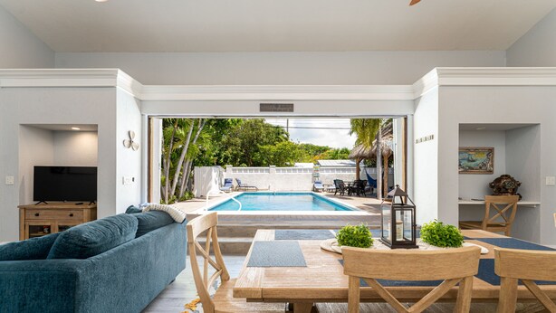 A pool area with a sofa and dining table, surrounded by white walls and a view of the pool. - SOUTHERNMOST SWIM AND SOCIAL CLUB  (Key West)