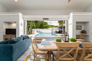 Ein Poolbereich mit einer Sitzecke und einem Esstisch, umgeben von weißen Wänden und Blick auf den Pool.