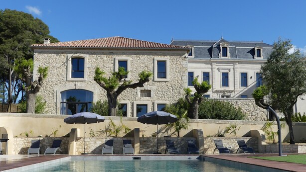 A stone building with a swimming pool, outdoor seating, and a well-maintained garden.