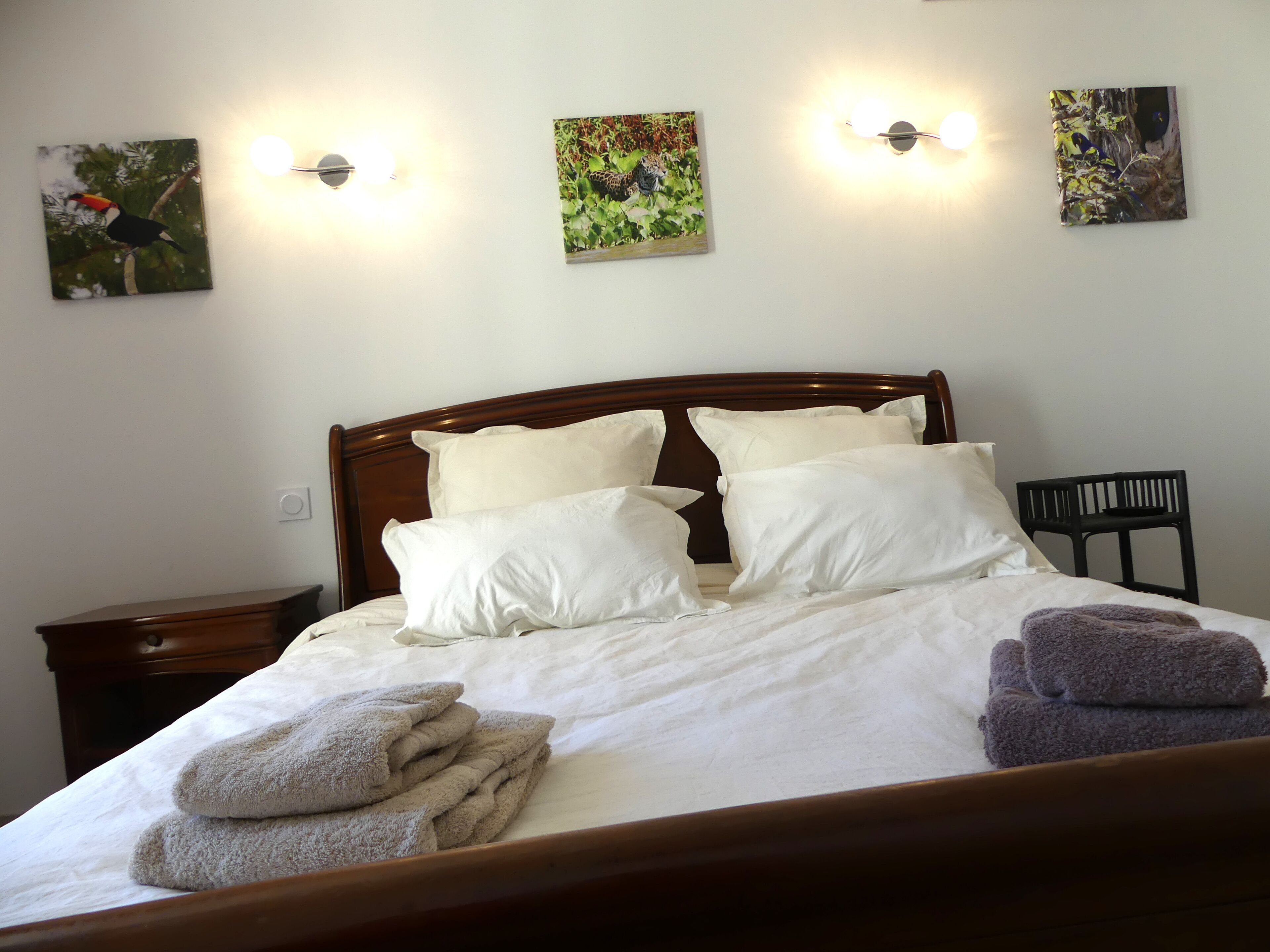 A neatly made bed with white linens and multiple pillows, a wooden headboard, and two wall-mounted light fixtures.